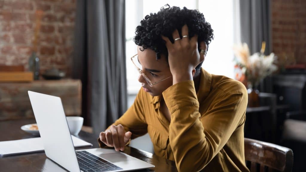 a woman with her hand on her head looking at a laptop