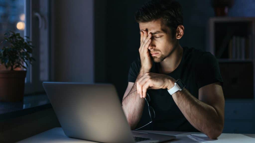 a man with his hand on his face looking at a laptop